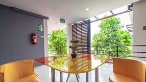Una sala de reuniones moderna con una mesa de vidrio, dos sillas amarillas, una planta en maceta y un extintor en la pared.