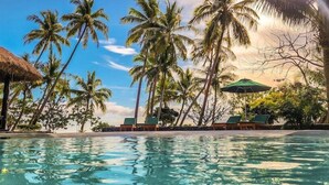 A pool area with lounge chairs and umbrellas, surrounded by palm trees. - Waya Island Resort (Yasawa Island)