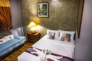 A hotel room with a bed, a sofa, a nightstand with a lamp, and a painting on the wall. - Huen San Fang Hotel (Fang)
