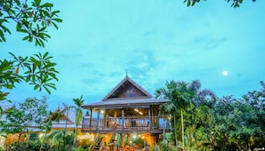 A traditional wooden building with a balcony, surrounded by lush greenery and palm trees. - Huen San Fang Hotel (Fang)
