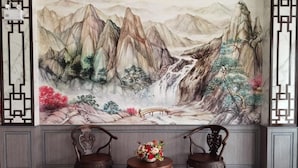 A room with a large traditional landscape painting on the wall, two ornate wooden chairs, and a small round table with a floral arrangement. - Chalalai Hotel Krabi (Nuea Khlong)