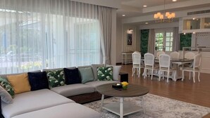 Un salon moderne avec un canapé d’angle, une table basse ronde et un coin repas avec des chaises blanches.