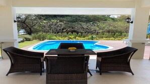 Un espace extérieur aménagé avec des sièges, une piscine, des fauteuils en osier et une table agrémentée d’un vase de fleurs.