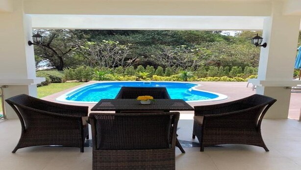 Un espace extérieur aménagé avec des sièges, une piscine, des fauteuils en osier et une table agrémentée d’un vase de fleurs.