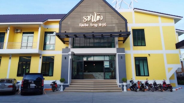 Un hotel moderno con fachada amarilla, un letrero llamativo que dice "Racha kong Hotel" y un estacionamiento con varias motocicletas.