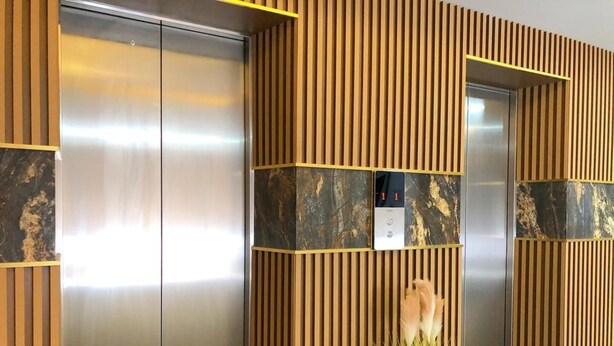 A modern elevator with a metallic finish, flanked by wooden paneling with vertical slats and marble accents. - Grandview Landmark Betong Hotel (Betong)