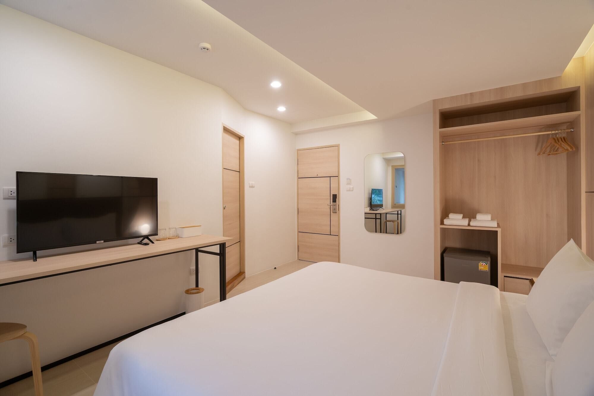 Una habitación de hotel moderna con una cama grande, un televisor de pantalla plana, un escritorio con ordenador, un armario y un espejo.