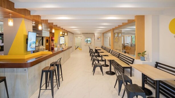 Un restaurant modern amb una barra llarga, diverses zones d'assaig i un interior lluminós.