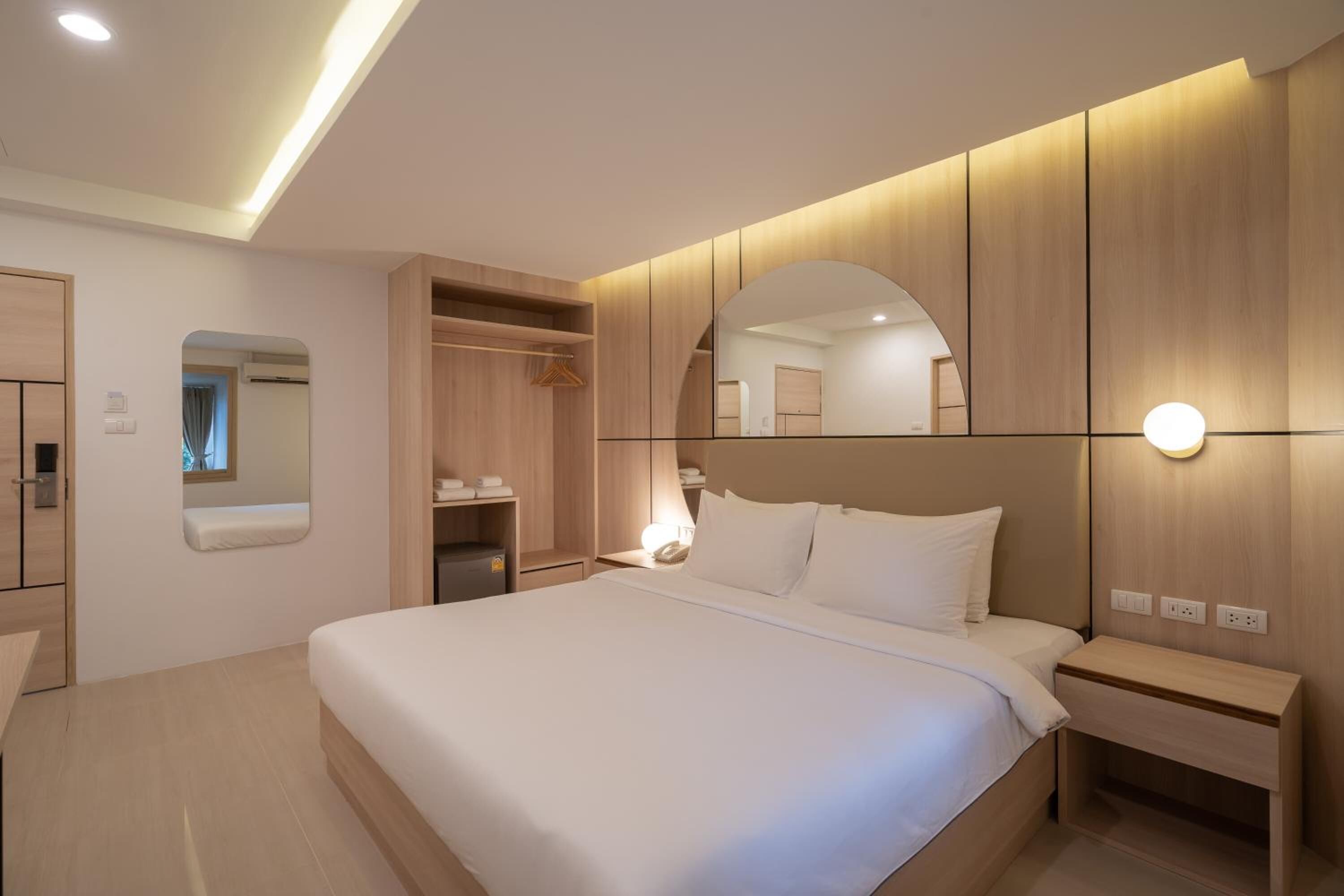 Una habitación de hotel moderna con una cama grande, armario empotrado, mesita de noche y un espejo.