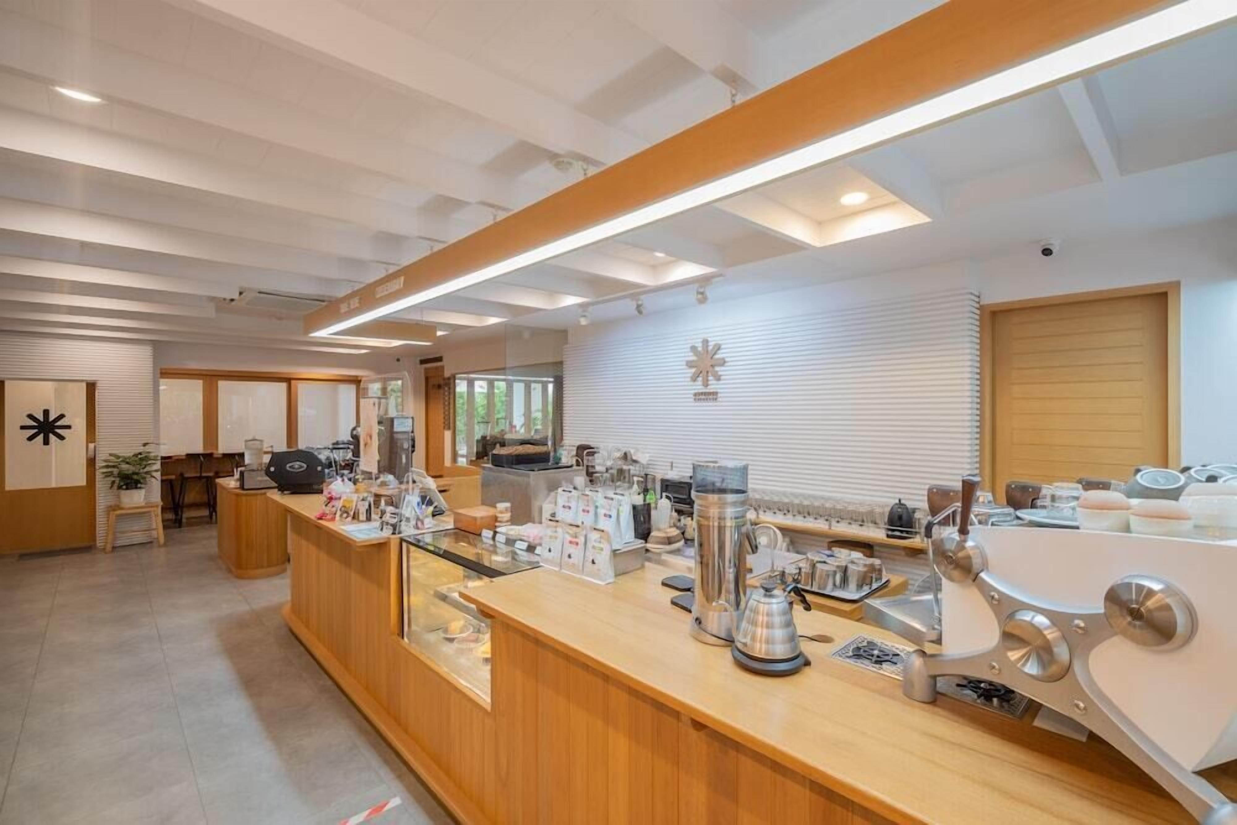 A modern coffee shop interior with a wooden counter, coffee machines, and a seating area with a view of the outdoors.