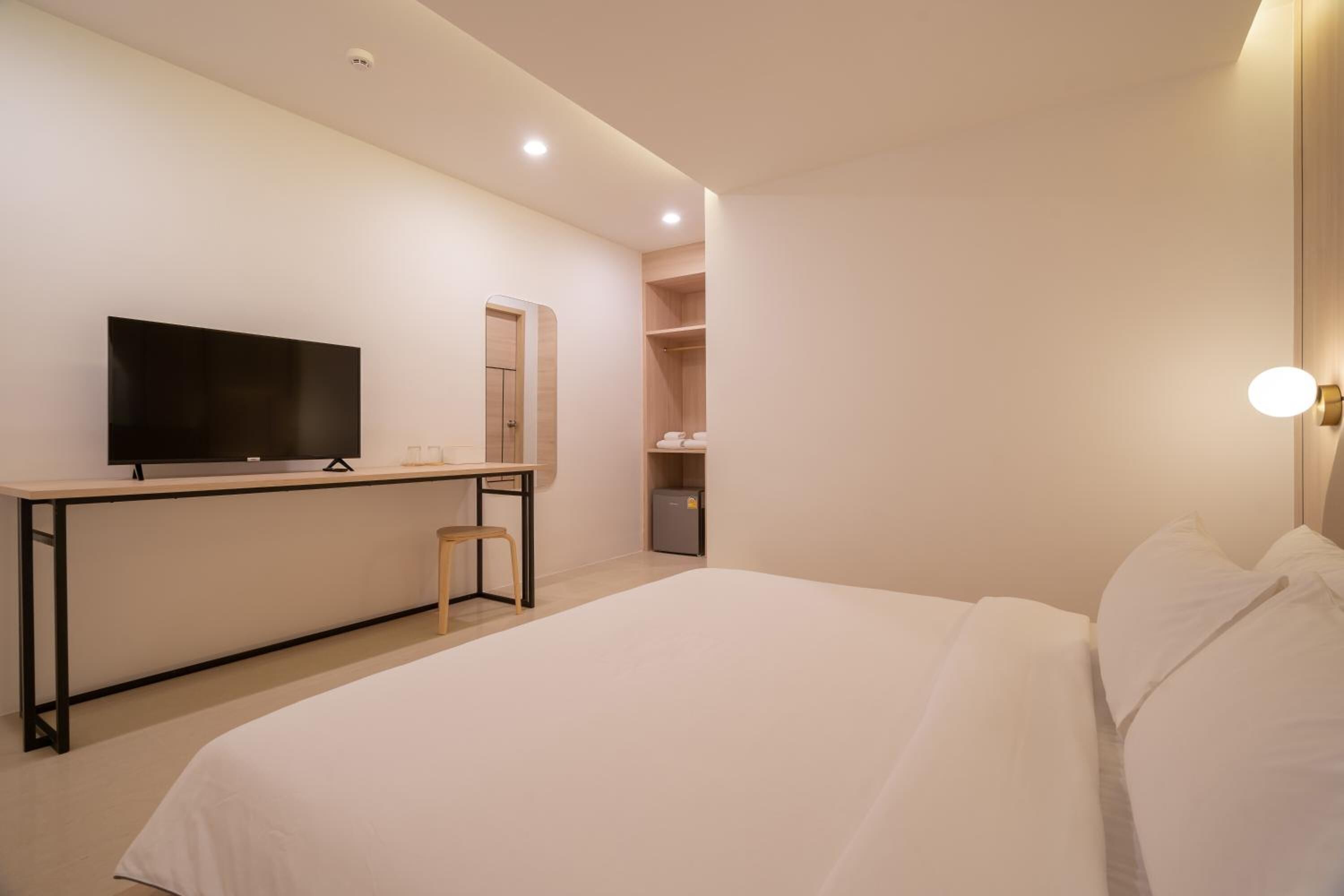 A bedroom with a bed, a desk, a television, a wardrobe, and a mirror.