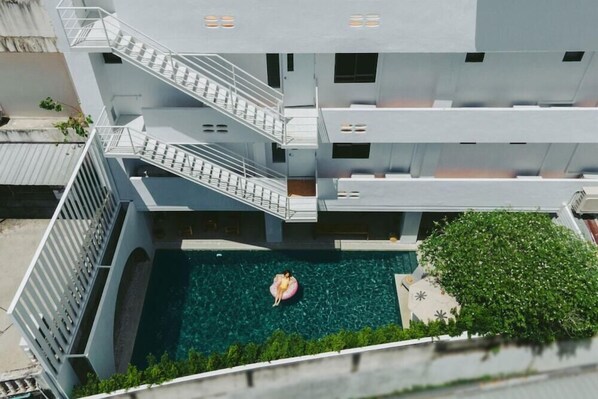 A modern building with multiple floors, a central courtyard with a swimming pool, and a staircase connecting the levels. - Bedline Hotel - SHA Certified (Phuket)