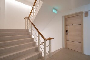 A staircase with white railings and wooden handrails, leading to a door with a light switch above it. - Bedline Hotel - SHA Certified (Phuket)