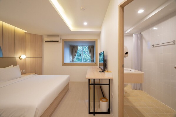 A hotel room with a bed, a desk with a computer, a window with a view, a shower, and a toilet. - Bedline Hotel - SHA Certified (Phuket)