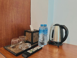 A wooden table with a tissue box, two water bottles, a kettle, a remote control, and a glass carafe. - Cokoon Deva Patong Hotel (Patong)