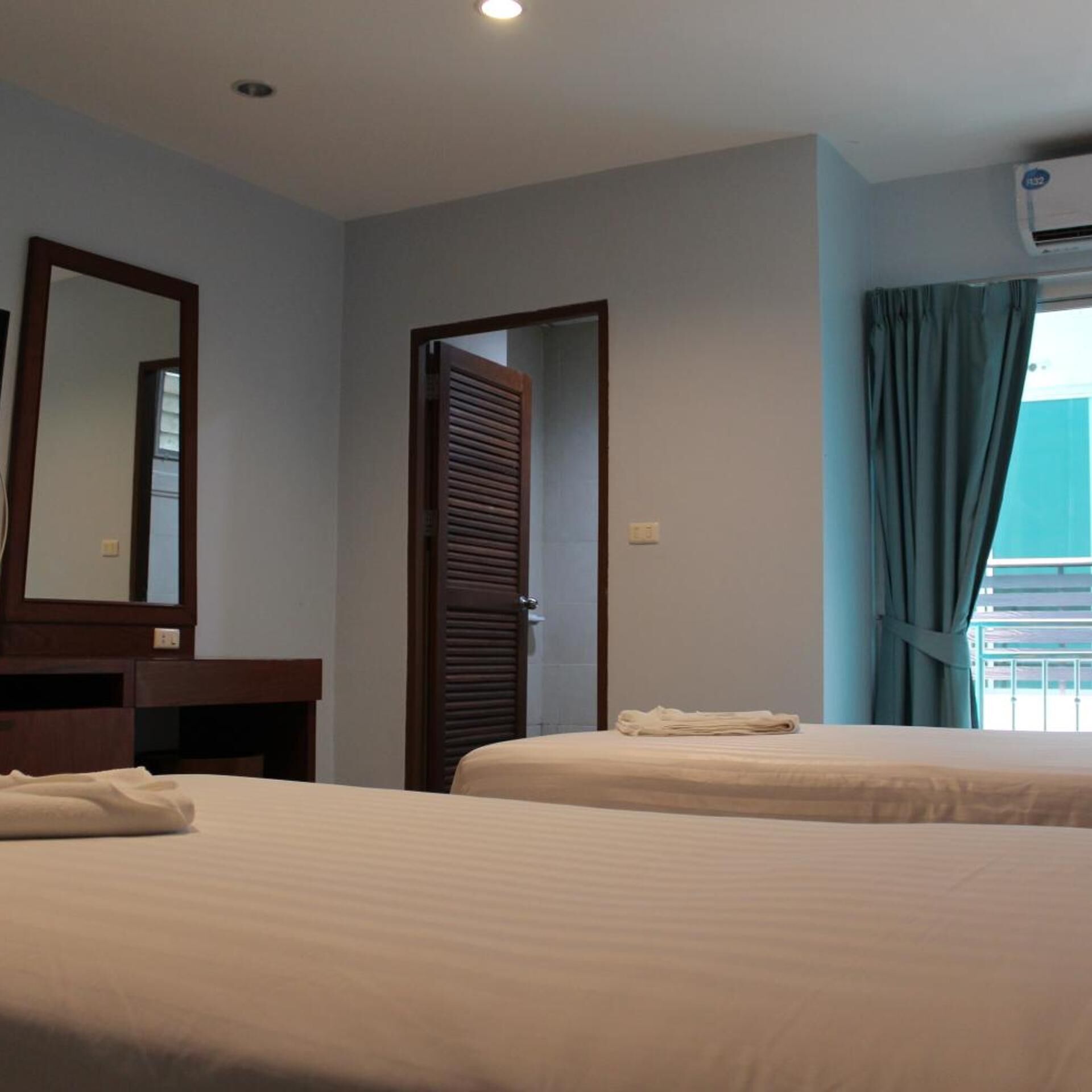 A hotel room with two beds, a mirror, a door, and an air conditioning unit.