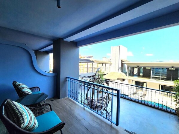 A balcony with a view of buildings, a chair with a cushion, and a metal railing. - Amalthea Hotel (Patong)