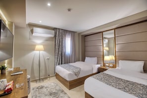 A hotel room with two beds, a flat-screen TV, a desk with a lamp, and a large mirror. - Nozol Pyramids Hotel (Giza)