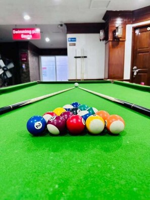 A pool table with a variety of colored balls and a cue stick, a sign indicating a swimming pool, and a door with a handle. - Lime Hotel Patong (Patong)