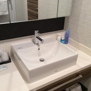 A bathroom with a white sink, a mirror, and toiletries. - Amand Hotel (Tokyo)
