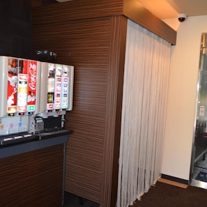 Un distributeur automatique de boissons, notamment du Coca-Cola, un mur recouvert de panneaux de bois et une porte en verre avec un rideau.