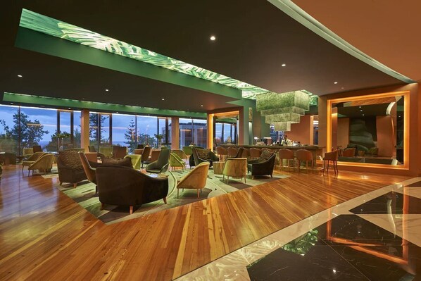 A spacious lobby with a wooden floor, comfortable seating, a bar area, and large windows offering a view of the outdoors. - The Reserve by Savoy Signature (Funchal)