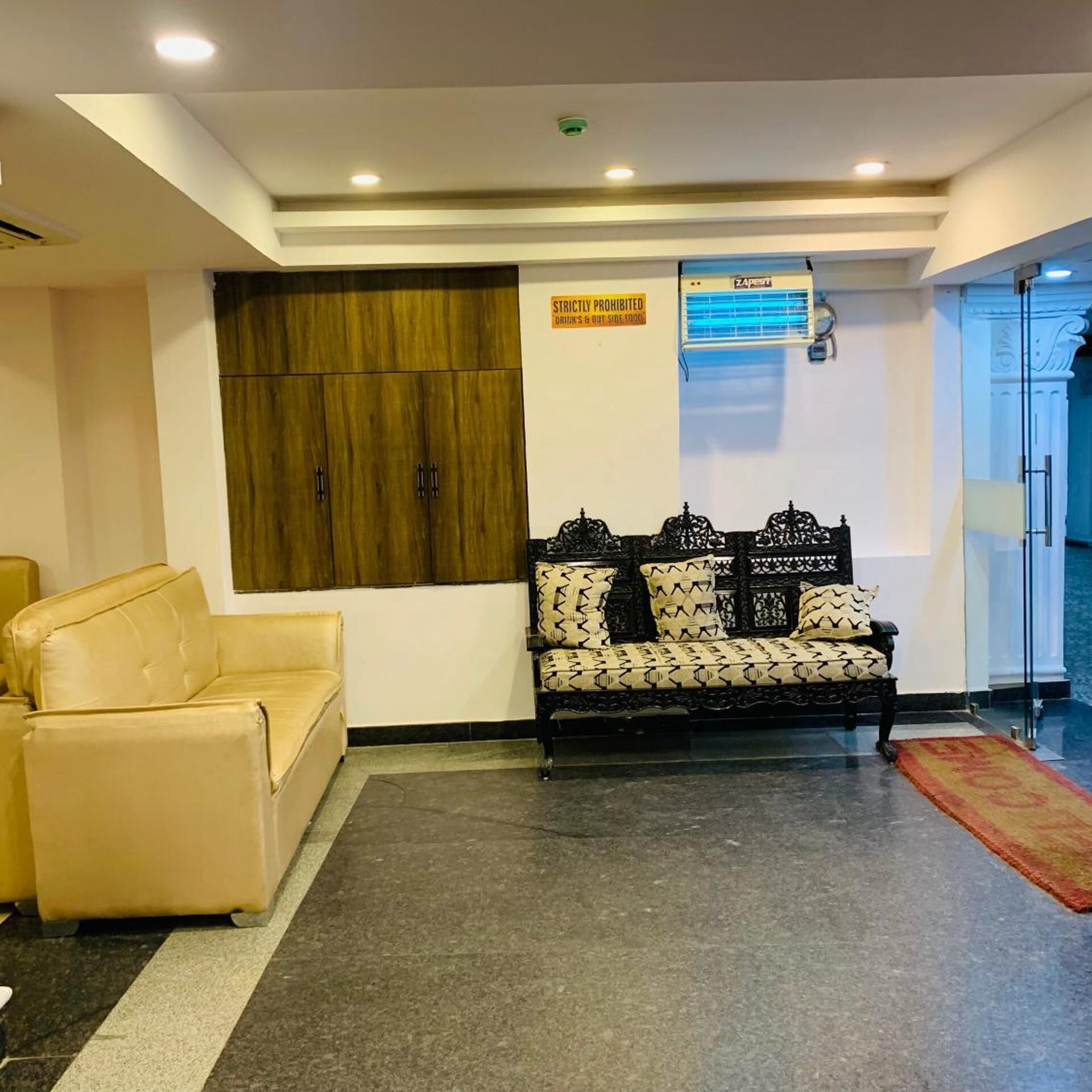 A lobby with a sofa, a leather armchair, a wooden wardrobe, and a sign prohibiting smoking.