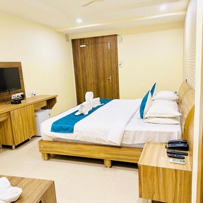 Ein Hotelzimmer mit Bett, Schreibtisch mit Fernseher, Kleiderschrank und Nachttisch mit Telefon und Fernbedienungen.