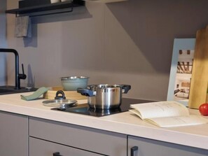 A modern kitchen with a stove, pots, a bowl, a book, and a red apple on the counter. - Candlewood Suites Dusseldorf Airport (Düsseldorf)
