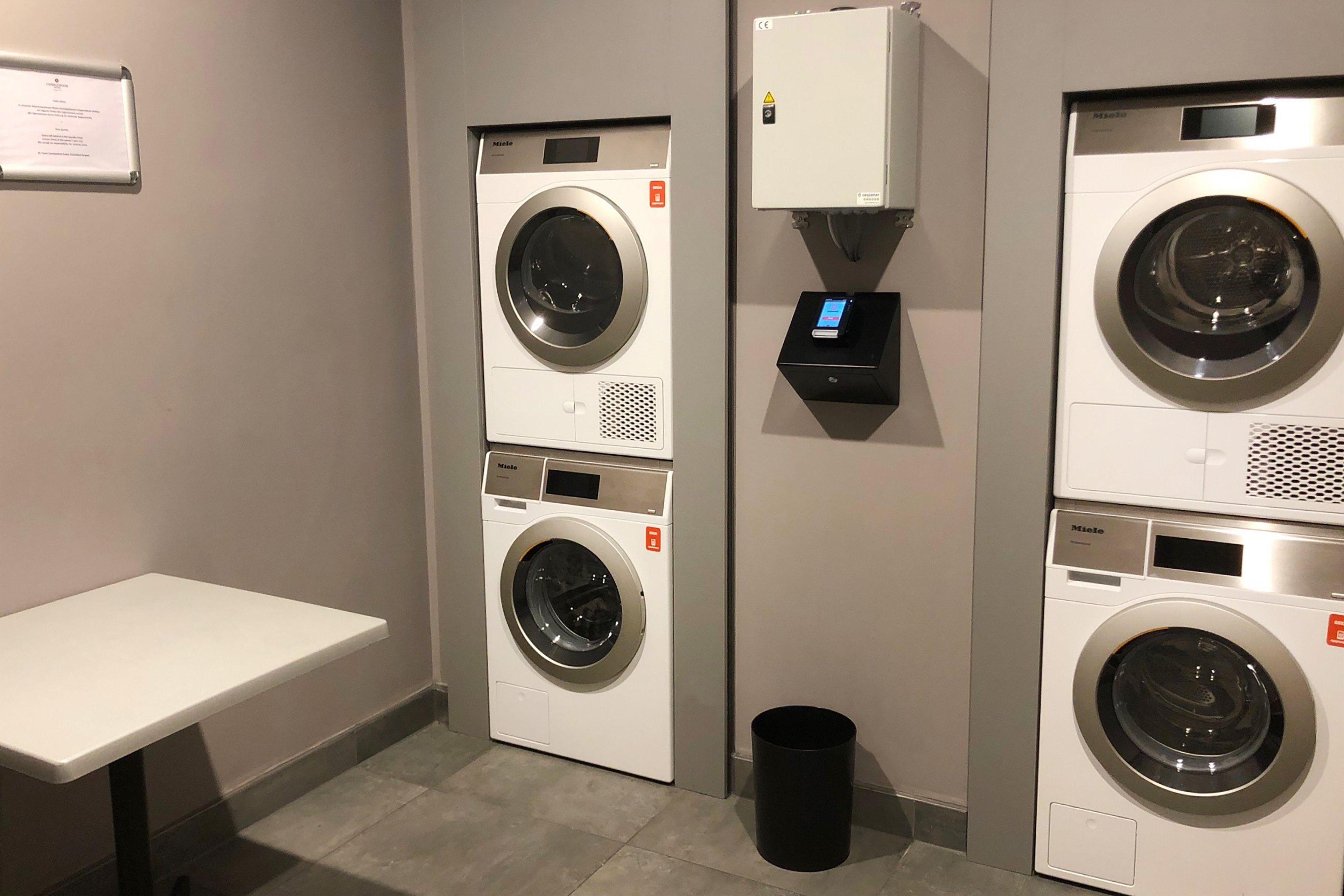 A laundry area with two front-loading washing machines, a small trash bin, and a control panel.