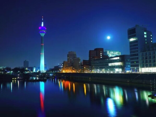 A city skyline at night with illuminated buildings and a tower reflecting on the water. - Candlewood Suites Dusseldorf Airport (Düsseldorf)