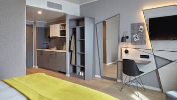 A modern room with a bed, a desk, a chair, a TV, and a kitchen area.