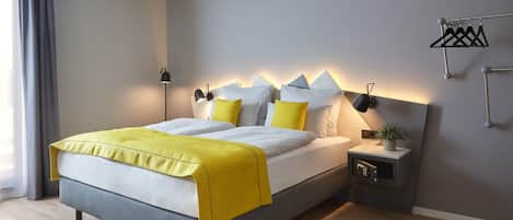 A modern hotel room with a bed, bedside table, lamp, and a wall-mounted towel rack.