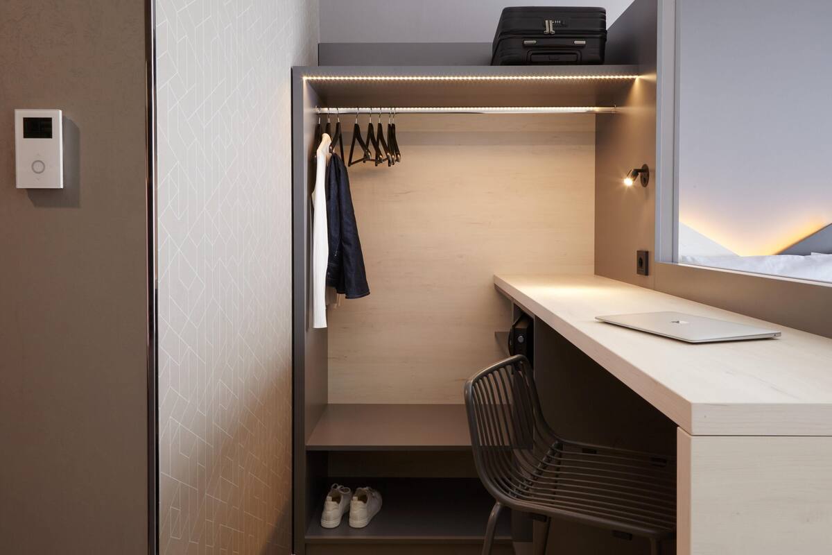A compact room with a desk, chair, and a hanging clothes rack.