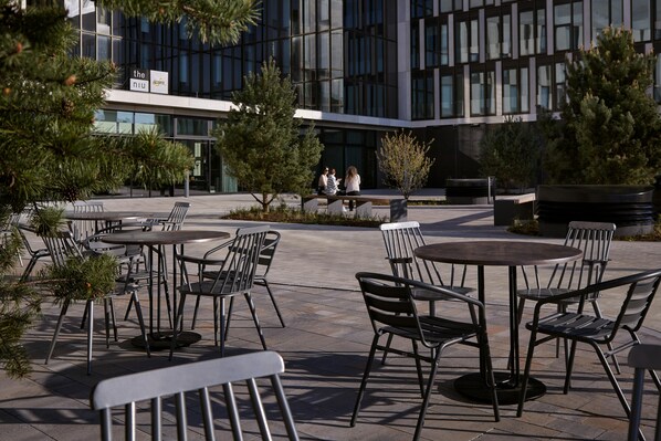 An outdoor seating area with tables and chairs, surrounded by potted plants and trees. - Candlewood Suites Dusseldorf Airport (Düsseldorf)