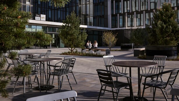 An outdoor seating area with tables and chairs, surrounded by potted plants and trees. - Candlewood Suites Dusseldorf Airport (Düsseldorf)