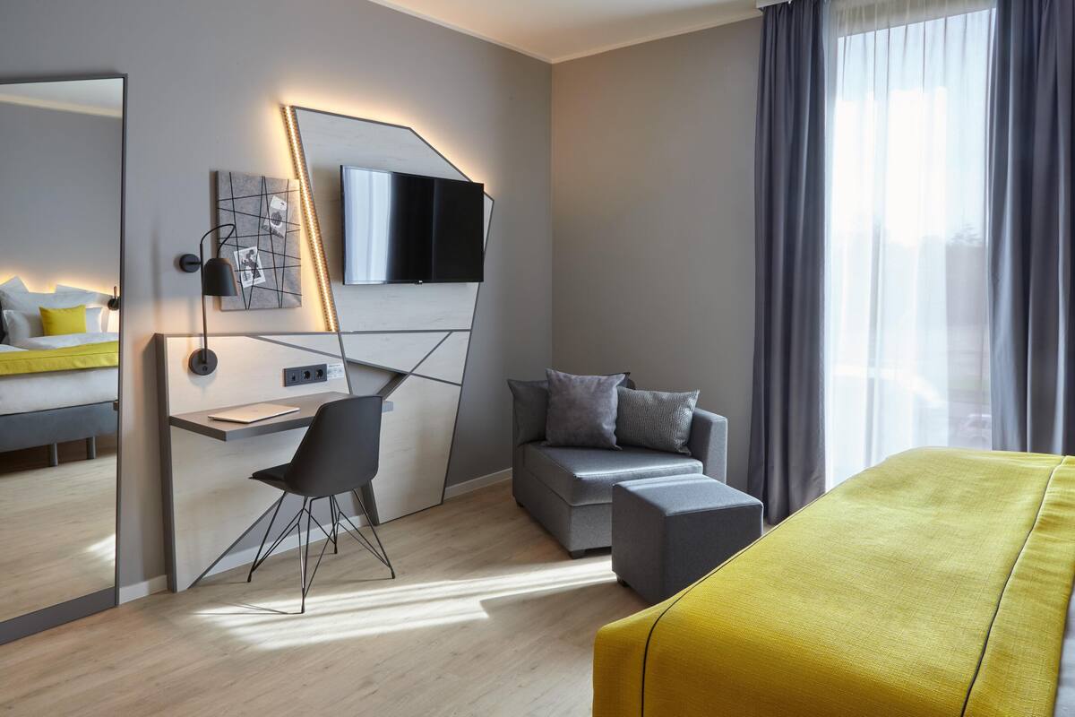 A modern hotel room with a bed, desk, chair, and a large window with curtains.