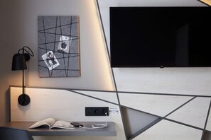 A modern hotel room with a flat-screen TV mounted on the wall, a bedside table with a lamp, and a power outlet. - Candlewood Suites Dusseldorf Airport (Düsseldorf)