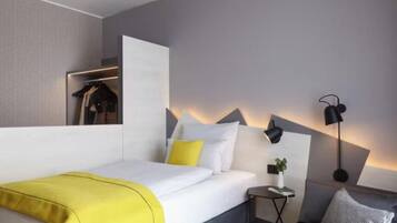 Ein modernes Hotelzimmer mit Bett, Nachttisch, Lampe und einer Couch.