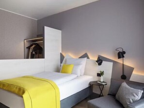 A modern hotel room with a bed, bedside table, lamp, and a sofa. - Candlewood Suites Dusseldorf Airport (Düsseldorf)