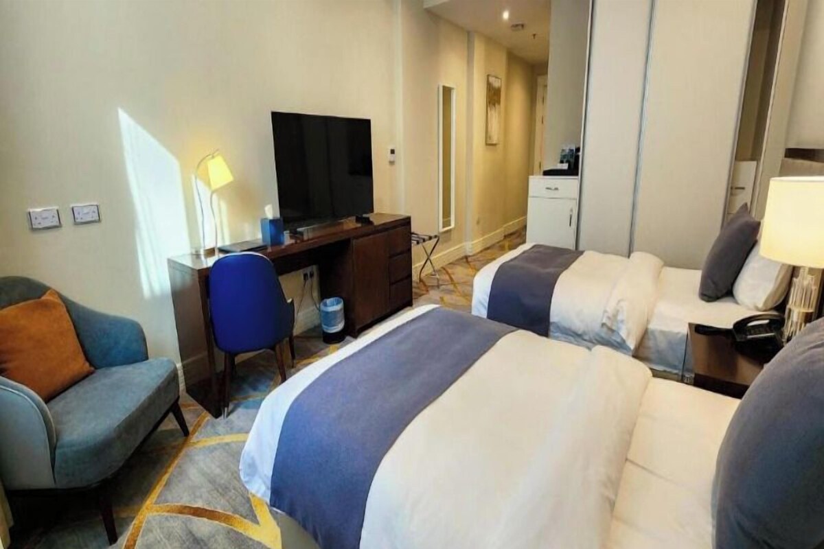 A hotel room with two beds, a desk with a computer, a chair, a TV, and a small cabinet.