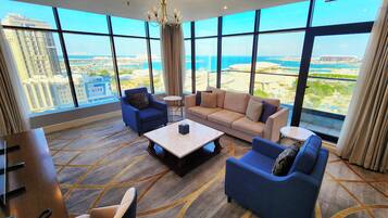 A hotel room with a large window, a sofa, a chair, a coffee table, and a desk.