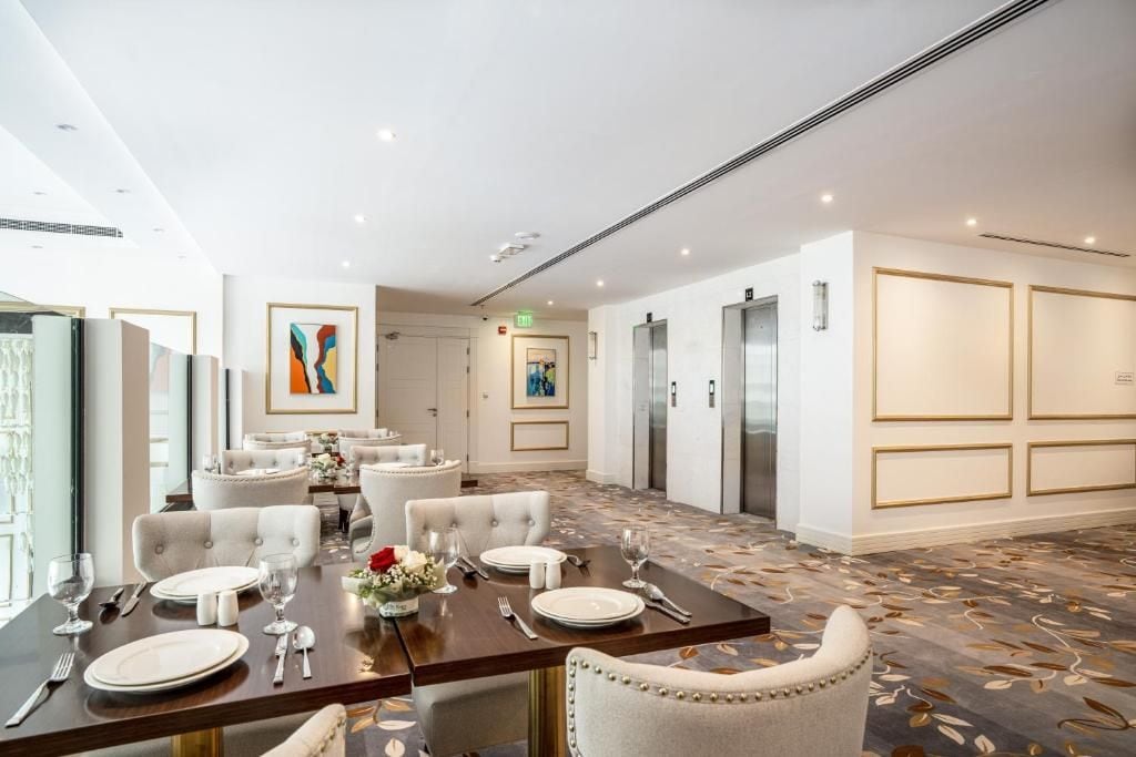 Un comedor de hotel con mesas dispuestas para el servicio, un cuadro abstracto grande en la pared y suelo alfombrado.
