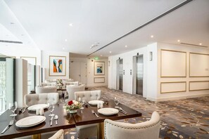 A hotel dining area with tables set for service, a large abstract painting on the wall, and a carpeted floor. - Shraao Hotel (Doha)