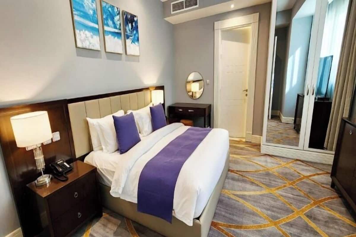 A hotel room with a bed, bedside table, lamp, and a mirror.