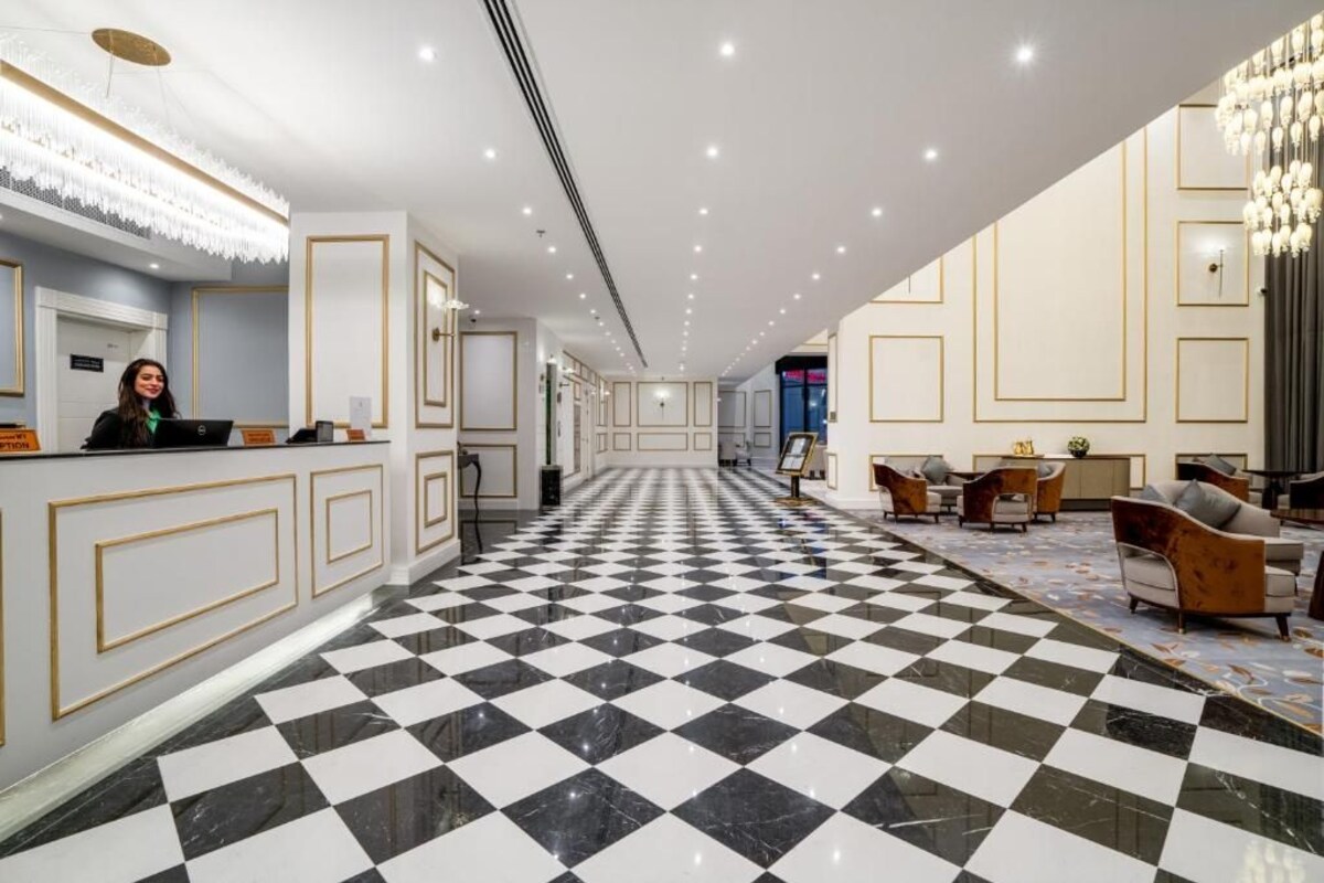 Um hall de hotel com piso xadrez, balcão de recepção e área de estar com sofás.