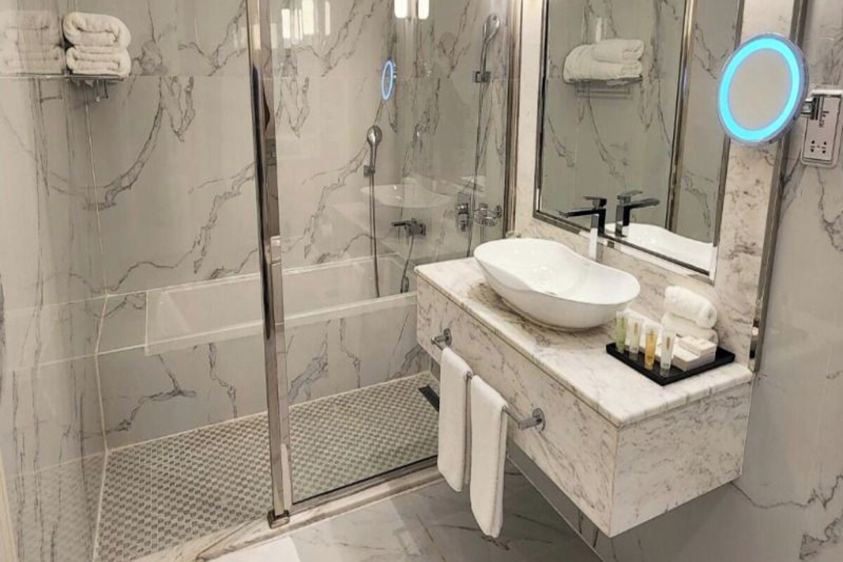 A modern bathroom with a glass shower enclosure, a white sink, and a large mirror with a blue light.