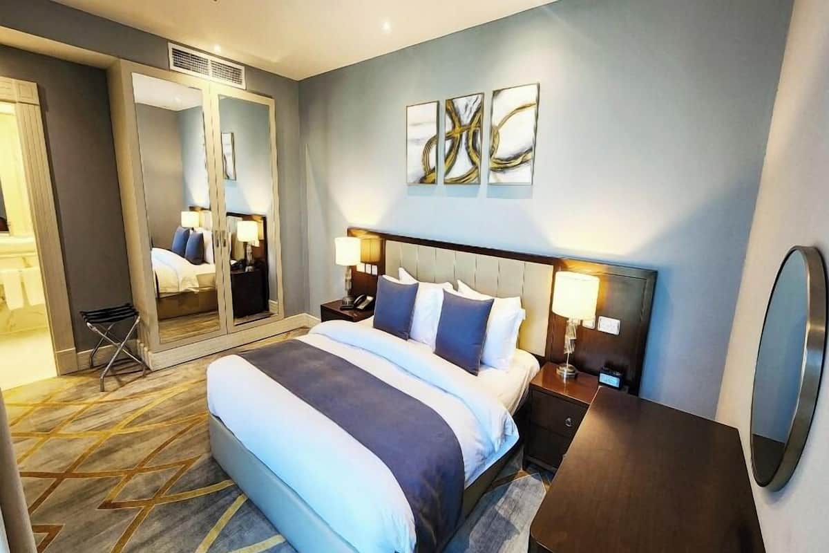 A hotel room with a large bed, bedside tables with lamps, a mirror, and abstract wall art.
