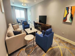 Una sala de estar moderna con un sofá, sillones, una mesa de centro, un televisor y un cuadro en la pared.