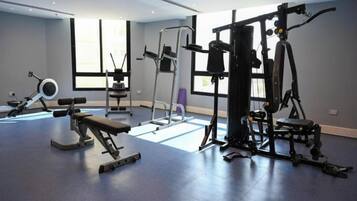 Un gimnasio con diversos equipos de ejercicio, amplias ventanas y piso azul.
